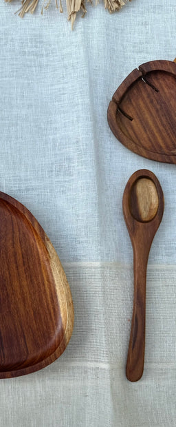 - Description: A wooden spoon with a rounded bowl and a long, slender handle. It sits on a light blue fabric backdrop, alongside round wooden plates or bowls.
- Audience and styling: Appears unisex; casual, rustic kitchenware styling suitable for home cooks.
- Materials and attributes: Made of wood with a smooth, polished finish; natural brown wood tones; simple, classic spoon design without handles or adornments.