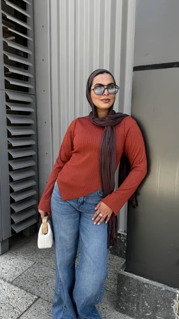 - What the product is: A modest-weight, rib-knit long-sleeve top in a warm cognac/terracotta color, paired with a scarf and wide-leg jeans, styled for everyday wear.
- Apparent audience: Women (based on the model’s styling, fit, and accessories).
- Notable attributes visible: Long-sleeve knit in a burnt orange cognac shade; high crew neck; relaxed, slightly oversized fit; paired with a dark patterned scarf and light-wash wide-leg denim; small light-colored handbag; sunglasses. Material appears to be knit fabric, likely cotton or blend, with a textured rib pattern. Color palette includes warm orange-brown top, dark scarf, and blue jeans.