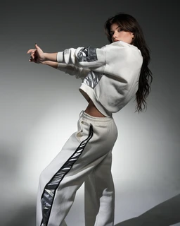 - What the product is: A metallic-trim tracksuit set consisting of a cropped white sweatshirt and matching jogger pants with metallic panels.
- Apparent audience: Women, based on the cropped fit, styling, and model.
- Notable attributes visible: White fabric with silver metallic panels along the sleeves and side stripe; cropped sweatshirt with long sleeves; high-waisted jogger pants featuring a metallic stripe/panel along the outer leg and a drawstring waistband; overall sporty, glossy metallic detailing with a sleek, modern look.
