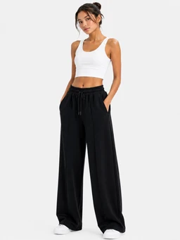 A pair of women's wide-leg trousers styled for a casual, athleisure-inspired look. The model wears a white cropped tank top with the black wide-leg trousers, which have a relaxed fit, drawstring waist, and side pockets, creating a comfortable, minimalist silhouette. The fabric appears lightweight with a smooth drape, in solid black, matching the Hashira fabric description.