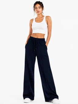 - What it is: A model wearing women's wide-leg trousers in a dark navy Hashira fabric, paired with a white cropped tank top and white sneakers. The pants feature a relaxed, loose silhouette with a drawstring waist and full-length wide legs.
- Intended audience: Women's.
- Notable attributes: Navy/dark indigo color, wide-leg cut, high-rise feel with a drawstring waistband, lightweight drape, plain front with side pockets, casual sporty styling. The fabric appears soft with a smooth finish.