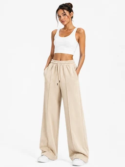 A pair of women's wide-leg trousers in a light, neutral beige color. The model wears a white cropped tank top, giving a casual, sporty vibe; the pants feature a high waist with an elastic drawstring and a relaxed, full-length silhouette. Visible materials appear to be a soft, drapey fabric with a smooth finish, suitable for a laid-back or loungey look.