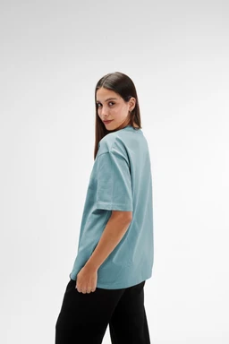 - Product: An oversized fit mint green T-shirt worn by a female model.
- Intended audience: Women (based on model styling and fit).
- Visible attributes: Mint green, short-sleeve, oversized silhouette with a relaxed drape, crew neck not clearly visible from side but typical T-shirt styling, lightweight knit fabric. The shirt falls loosely past the hips, paired with dark bottoms. No visible branding or logos.
