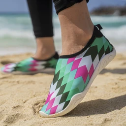 This is a slip-on water-friendly shoe with a geometric diamond pattern in green, pink, white, and black. It appears designed for a unisex or womenโs audience, based on the shoeโs sleek, low-cut silhouette and flexible fabric upper. Notable attributes include a bright, multicolor zigzag motif, a soft black collar, and a light, grippy sole suitable for beach or poolside wear.