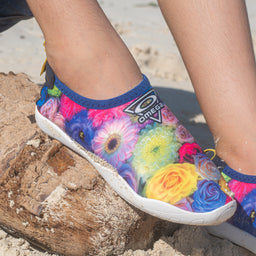 - What the product is: A casual slip-on water shoe for beach or pool use, featuring a low-cut design with a flexible, rubber-like sole.
- Apparent audience: Unisex or boys/girls depending on size; shown on a child’s foot, suggesting a kids' size.
- Notable attributes: Bright floral print in vibrant colors (pink, yellow, blue, green) with a blue trim and a white sole; lightweight upper material that looks quick-drying and mesh-like, with a logo patch on the side.