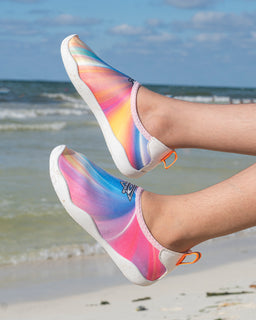- A pair of slip-on water shoes with a vibrant rainbow gradient design, shown worn on feet and lifted in the air on a beach background.
- Audience: unisex (appears suitable for both men and women, kids not clearly indicated).
- Notable attributes: multicolor gradient (pink, orange, purple, blue), white sole and trim, low-cut casual water-shoe style with pull tabs on the heel. Material suggests a flexible, quick-dry fabric upper with a rubber-like sole.