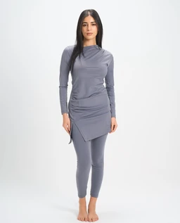 A women's swim set featuring a long-sleeve, high-neck top paired with matching leggings in a soft grey. The top has a draped, asymmetrical wrap hem that creates a layered effect at the hip, and the full-length leggings offer a sleek, fitted silhouette. Notable materials appear to be a stretch knit/swim fabric with a smooth, matte finish in a cool grey tone.
