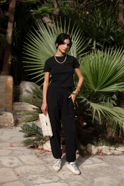 - What the product is: A coordinated two-piece set consisting of a fitted short-sleeve black top and matching high-waisted black relaxed pants.
- Apparent audience: Women (model styling, slim fit top with casual yet polished look, suitable for womenswear).
- Notable attributes: Black solid color, short-sleeve crew neck top, drawstring/elastic waist pants, relaxed straight-leg fit, paired with light sneakers and a small handbag. Fabric texture appears smooth and soft, with a minimal, chic style suitable for casual to smart-casual occasions.