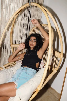 - Product: Luna Top (visible worn by model in the photo)
- Audience: Women's (styled and fitted for a female figure)
- Visible attributes: black sleeveless top with a high neckline and side cut-out detailing, paired with light-wash distressed denim shorts. The model sits in a hanging wicker chair, suggesting a casual, chic summer vibe. No brand logos visible, focus remains on the garment’s cut and fit. Material appears to be a smooth, stretch fabric. Color is solid black.