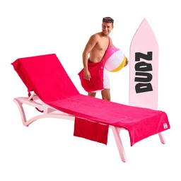 - The product is a pink beach lounge set with a reclining chaise and matching pink towel/cover, shown with a man in swimwear holding a pink-and-white ball and a pink surfboard flag in the background.
- Intended audience: unisex (appears as a beach/relaxation setup suitable for adults, but styled on a man in swimwear).
- Notable attributes visible: bright pink color dominating the chaise and towel, white plastic frame, curved lounge design, and an accompanying pink surfboard-like flag with black lettering. The scene suggests a tropical, water-side leisure style.