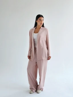 This is a women’s lounge suit set consisting of a relaxed blazer and wide-leg pants in a soft rose-pink linen fabric. The model wears a white or light top underneath, giving a casual yet refined look suitable for home wear or casual outings. Notable attributes include the breathable linen material, pale rosy color, oversized blazer silhouette, and loose, comfortable fit.