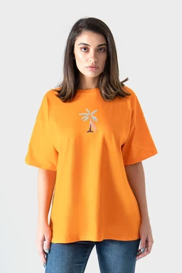 A bright orange oversized T-shirt featuring a small palm tree print at the chest. The model appears to be a woman, with a relaxed, loose fit and mid-length sleeves that drape casually. Notable details include the bold solid color and simple tropical graphic, with a soft, jersey-like fabric appearance.