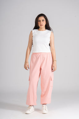 This is a sleeveless ribbed crew-neck tank top worn by a female model. The intended audience appears to women, judged from the styling and fit. Visible attributes: white ribbed knit fabric, crew neckline, sleeveless cut; paired with light pink wide-leg cargo-style pants and white sneakers, giving a casual, sporty look.