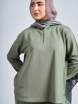 - What the product is: A light olive-green pullover with a half-zip neck, shown worn by a female model. The top has a relaxed, athletic fit and a subtle textured or waffle-like fabric.
- Apparent audience: Women's or unisex, based on the styling and fit on a female model; long sleeves and modest cut suggest everyday casual wear.
- Notable attributes: Olive/khaki color, long-sleeve pullover with a zippered stand collar, lightweight, breathable fabric with a small brand tag near the hem, and a loose, comfortable silhouette.