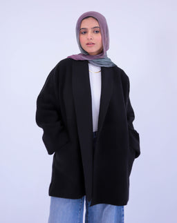 - What it is: A loose, open-front wool jacket in black, worn over a light top, with hands in pockets.
- Intended audience: Appears unisex or aimed at women (based on the relaxed, oversized silhouette and styling with a hijab).
- Notable attributes: Material appears wool or wool-blend; solid black color; oversized, relaxed fit with wide sleeves and a minimal, clean front with no visible closures. Styling is casual yet polished, worn with a light-colored headscarf and layered look.