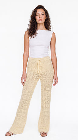 This is a knit beach pants/trouser style, shown on a female model, designed for women. The pants are cream/beige with a crochet-like knit pattern, a drawstring waist, and a wide-leg silhouette that reaches the floor. The look is casual, warm-weather, with a soft, textured fabric and open, lace-like knit detailing.