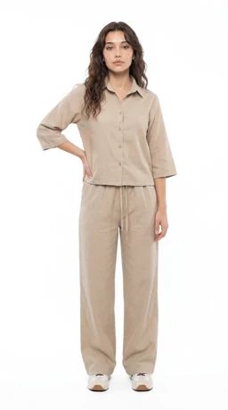 - What the product is: A matching linen set consisting of a button-up shirt and wide-leg pants in a light beige color.
- Apparent audience: Women's (model shown is female, with styling and fit suggesting a women’s size).
- Notable attributes: Light, natural linen-like fabric in a beige/tawnish tone; relaxed, loose fit with a collared shirt featuring three-quarter sleeves and a drawstring-waisted, wide-leg pant. Simple, minimal styling with white sneakers.