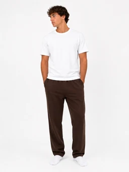 - What the product is: A man wearing a casual outfit consisting of a plain white T-shirt and dark brown regular-fit sweatpants. 
- Apparent audience: Menswear (unisex styling is minimal, but the model and fit suggest men’s sizes and styling).
- Notable attributes: The T-shirt is short-sleeved and crew-neck; the pants are brown, loose through the legs with a relaxed/regular fit, likely fleece or jersey material typical of sweatpants. The look is simple and minimal, with white socks visible. No branding shown.