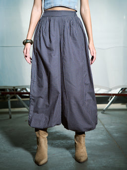 - Description: A pair of navy checkered balloon pants with a wide, loose fit through the legs and a gathered, elasticized waistband. The hem is cropped above the ankle, creating a voluminous silhouette.

- Intended audience: Women (based on the styling with a cropped top and ankle boots).

- Notable attributes: Navy micro-check pattern, balloon leg style, gathered waistband, cropped length, and relaxed drape with structured volume. Material appears lightweight fabric with a soft, matte finish. Color palette is navy and white.