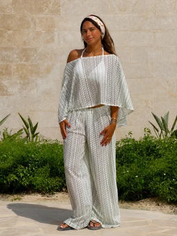 A coordinated loungewear set featuring a light sage green/white print. The outfit includes an off-the-shoulder, flowy cropped top with wide sleeves and matching wide-leg pants, both loose and relaxed in fit. The visible material appears soft and lightweight, likely a breathable fabric with a subtle dotted/mini-pattern. Styling suggests a beachy, coastal vibe with a headband/accessory and simple sandals. Audience appears to women; colors are sage green and white with a comfortable, breezy silhouette.