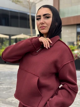 This is a burgundy quarter-zip sweatshirt with a relaxed, oversized fit. The model appears to be a woman, wearing a black headscarf, and the garment features a half-zip collar with a zip pull and large front pocket detailing; the fabric looks like a thick fleece or sweatshirt knit in a matte finish. The color is a rich wine/burgundy, and the style leans casual, sporty loungewear.