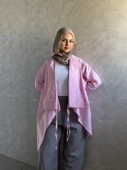 A women's cardigan-style outer layer in soft pink with an open front and draped, asymmetrical hem that ties at the waist. The model wears a light gray hijab and a white top, paired with loose gray pants, giving a modest, casual look. Notable attributes: pale pink color, lightweight fabric, long sleeves, and a relaxed, waterfall cardigan silhouette.