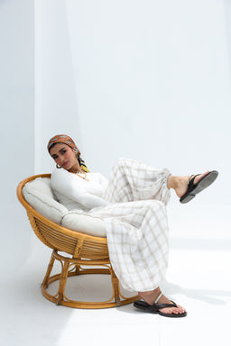 - What the product is: A pair of beige balloon-style trousers displayed on a model seated in a wicker chair.
- Apparent audience: Women's fashion (unisex look but styling and fit suggest women's trousers).
- Notable materials, color, and style attributes: Light beige, soft flowy fabric with a balloon/expanded leg silhouette, high waist feel, paired with a white top and black sandals. The overall style is relaxed, lounge/awake-at-home chic. Visible texture suggests a smooth, lightweight material.