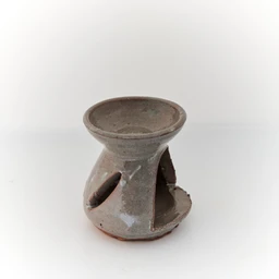 This is a small, handmade ceramic diffuser holder with a hollow, open-bottom design. It appears unisex in style, crafted from grayish, matte clay with a rustic finish and a shallow dish on top for essential oils or atomizer scents, plus cutouts on the sides for airflow. The visible attributes include a light gray-brown ceramic material, a wide top reservoir, and curved openings that give it a simple, earthy, artisanal look.