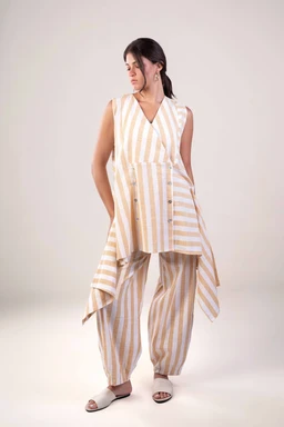 - Description: A sleeveless, v-neck striped linen set consisting of a long, asymmetrical front-zip style top with a layered hem and matching wide-leg, cropped pants. The stripes are in light yellow and white with a relaxed, drapey silhouette.
- Intended audience: Women.
- Visible materials/colors/style: Striped yellow and white linen fabric, lightweight and breathable with a soft, flowy, casual summer vibe; flat open-toe sandals styled for a breezy, resort-inspired look.