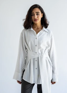 This is a white wrapped shirt-dress with a casual, oversized fit. It features a button-down front, a collared neckline, long sleeves with wide cuffs, and a self-tabric belt tied at the waist for a cinched silhouette. The visible material appears lightweight and slightly textured, with a soft, starlight-like white color; the styling leans toward women’s fashion. Material hints at a soft woven fabric, with a relaxed yet polished look.