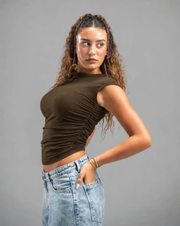 - What the product is: A fitted short-sleeve brown top with ruching along the sides, styled on a female model.
- Apparent audience: Women's apparel, based on the cut, styling, and sizing fit.
- Notable attributes: Dark brown/olive hue, crew neckline, ruched side detailing at the torso, cropped length, paired with light-wash denim jeans.