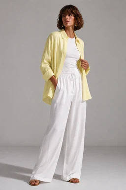 - What it is: A bright yellow lightweight shirt worn open over a white top and white wide-leg linen pants. The shirt appears relaxed-fit with a soft, breathable look.
- Audience and styling cues: Appears designed for women (model is female); styled in a casual, airy outfit suitable for warm-weather or resort wear.
- Visible material, color, and style: Materials look like soft linen or linen-blend. Colors are yellow shirt, white top, and white wide-leg pants. The overall style is casual, relaxed, and comfortable with an oversized shirt layering over a simple sleeveless or short-sleeve top.