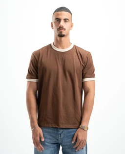A brown short-sleeve tee with contrasting light beige/cream trim at the neck and sleeve cuffs. The fit appears standard and masculine, modeled by a man with a clean, minimalist styling. Notable details: solid brown fabric, cream-colored ribbed trim, crew neckline, and casual everyday tee vibe.