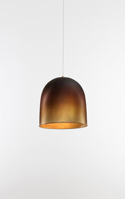 This image shows a single pendant light with a dome-shaped shade in an oxidized, gradient bronze finish. It appears designed for a unisex or general audience, hung from a thin cord against a plain white background, with a warm inner glow suggesting a warm-toned bulb. Notable attributes: oxidized metallic finish, smooth curved dome, and a minimalist hanging pendant style.