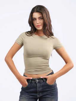 - Product: Comfy Stretch Cotton Top. A fitted, short-sleeve tee in a light beige/taupe color with a crew neckline, shown on a female model.
- Audience and styling cues: Appears designed for women; the top is cropped and form-fitting, styled with high-waisted jeans for a casual, everyday look.
- Notable attributes: Material appears soft, stretch cotton; solid neutral color; cropped length with ruched sides creating a ruched effect at the torso.