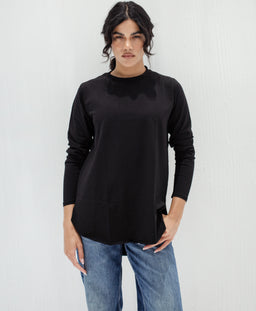 Description:
- A loose-fit black long-sleeve top with a round neckline, shown on a female model. The shirt has a simple, minimalist basic style with a slightly curved hem and standard cuffed sleeves. The fabric appears smooth with a matte finish, likely a knit or lightweight jersey. The model pairs it with blue jeans for a casual, unisex-leaning look. Notable attributes: solid black color, long sleeves, crew neck, relaxed silhouette, and soft drape.