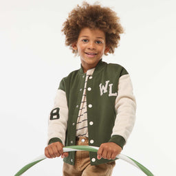 - A child wearing a varsity-style jacket in khaki and dark green. The jacket features contrasting light sleeves, green cuffs, hem, and collar, with snap buttons down the front and large “WL” lettering on the left chest and a number patch on the left sleeve.
- Apparent audience: children's (youth/ kids) based on the model.
- Notable materials and style: knit-style varsity jacket with wool-like body, cotton/knit sleeves, two-tone color scheme (khaki body with cream sleeves), bold lettering and sporty varsity aesthetic.