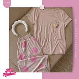 - What it is: A women's pajama set consisting of a short-sleeve T-shirt and matching pants, shown in a soft beige-pink tone with pink tie-dye accents on the pants.
- Audience and styling cues: Designed for women, with a relaxed, comfortable loungewear look. The shirt features a small fruit graphic on the chest, and the pants have an elastic waistband and pink tie-dye spots.
- Material, color, and style notes: Appears to be a soft cotton or cotton-blend fabric in a beige/peach color. The overall style is casual/modern loungewear with a pastel color palette and playful fruit-themed motif.
