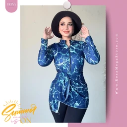 - What the product is: A blue patterned long-sleeve tunic or swim cover-up with a waist tie, worn as a modest outer layer.
- Apparent audience: Women, based on the model and styling (hat and fitted silhouette suitable for adult female wear).
- Notable attributes: Blue fabric with a white marble-like print, front zipper, high collar, belt/tie at the waist creating a gathered silhouette, paired with dark pants. The look is casual yet stylish, suitable for resort or beachwear as a burkini cover. Material appears lightweight and flowy.