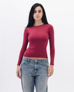 - What it is: A fitted, long-sleeve top in a deep red/magenta color with a crew neckline, shown on a female model.
- Intended audience: Women (based on styling and cut).
- Notable attributes: Stretchy, smooth knit fabric with a body-hugging silhouette; solid color; ribbed-like stretch at cuffs; pairings suggested with casual denim (as shown).