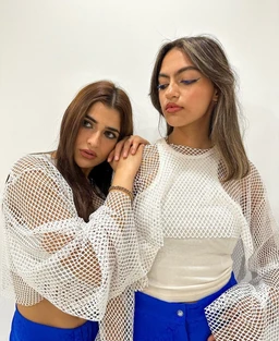- A pair of women modeling a sheer, white fishnet top with oversized, lattice-knit sleeves. They wear it over light-colored tops, creating a high-contrast, airy look.
- Audience: unisex or women’s, based on styling and fit shown (cropped, form-flattering). 
- Notable attributes: white fishnet mesh, oversized bell sleeves, cropped length, layered with solid underlayers; casual, edgy, clubwear vibe. No brands or logos visible.