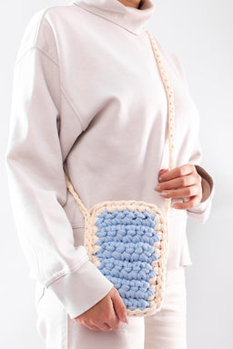 - What the product is: A small turquoise mini crochet bag with a chunky textured crochet front panel, worn crossbody over a light sweater.
- Intended audience: Unisex appeal for a casual, boho/handmade style look (shown on a female model).
- Notable attributes visible: Light cream/beige crocheted strap and edging, soft pastel turquoise front panel, compact rectangular shape, open-top design implied by crochet texture; overall mini size suited for small personal items.