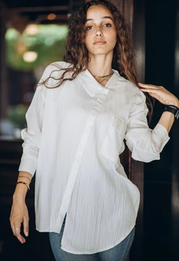 - Product: White shirt with a relaxed oversized fit and a soft, lightweight texture.
- Audience: Women's (based on styling and fit on the model).
- Notable attributes: Crisp white color, long sleeves, high-low curved hem, hidden placket, collared neckline; appears slightly sheer with a subtle vertical stripe texture. Casual, versatile shirt suitable for everyday wear.