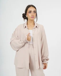 Description: A model wears a loose, oversized shirt and matching pants set in a soft beige crinkle linen fabric. The look is relaxed and unisex in silhouette, with long sleeves gathered at the cuffs and a button-front shirt paired with wide-legged pants.

Audience and materials: Appears suitable for women (based on model styling). Notable attributes: light beige color, crinkle linen fabric, oversized/relaxed fit, button-down shirt, and matching wide-leg pants with elasticized or smocked detail at the waist.
