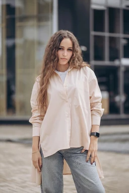 - Product: A light, long-sleeve cotton blouse with a high-low hem and visible sheer elements along the placket area; oversized pocket detail on the front.
- Audience: Women's (model styling with relaxed fit and soft tones suggests a feminine, casual-to-smart look).
- Notable attributes: Soft beige/cream color, cotton fabric, oversized silhouette, button-down front, high-low hem, and a prominent front pocket.