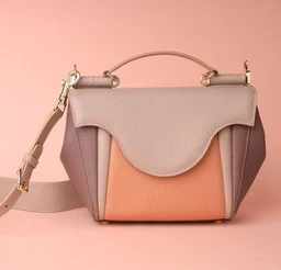 - Product: A small crossbody/handbag with a structured, compact silhouette and a top handle.
- Audience: Unisex-leaning toward women based on styling and size, but can be used by any gender who prefers a handbag.
- Visible attributes: The bag features color-blocked panels in nude, peach, and taupe tones with a pebbled leather texture. It has a curved flap front, a contrasting front pocket under the flap, a short top handle, and a detachable shoulder strap. Gold-tone hardware accents the strap attachments. Overall style is chic, modern, and geometric.