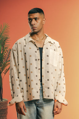 - What the product is: A light beige linen shirt with an allover embroidered pattern and a front chest pocket, shown worn over a dark inner top.
- Apparent intended audience: Men (adult male model, relaxed casual fit).
- Notable attributes: Linen fabric with a natural, textured beige color; embroidered motifs in darker tones; button-front with a collar and a single chest pocket; loose, slightly oversized fit with long sleeves.