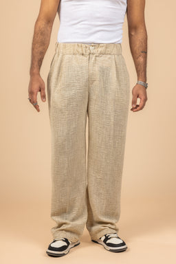 - What the product is: Tailored Linen Pants in beige.
- Apparent audience: unisex or men's style pants, based on the model and cut.
- Notable attributes visible: light beige linen fabric with a textured weave, relaxed tailored fit, elastic waistband with a drawstring, side pockets, full-length with a loose, straight leg, paired with a white sleeveless top and sneakers for a casual look.