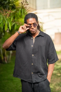 - A loose, oversized short-sleeve shirt in black with a button-front placket and a relaxed fit.
- Appears aimed at men (adult model), with a casual, streetwear vibe supported by the dark color, roomy cut, and rolled sleeves.
- Notable features: breathable cotton fabric, black hue, mid-length hem, and light collar with large buttons.