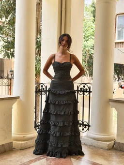 - What the product is: A full-length, black tiered dress with multiple ruffled layers and a fitted bodice.
- Apparent audience: Women (styled on a female model with a strapless, corset-like neckline and slim silhouette).
- Notable attributes: Black fabric with white polka dot pattern, spaghetti straps, sweetheart/strapless neckline, multiple horizontal ruffled tiers creating a voluminous, floor-length skirt; appears to be made from lightweight, flowy material suitable for formal or evening wear.